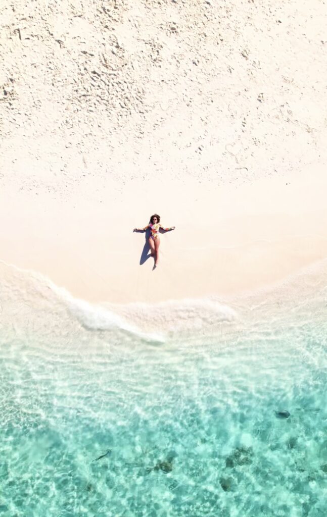 Mujer acostada en la arena de una playa paradisíaca con el mar cristalino a su lado