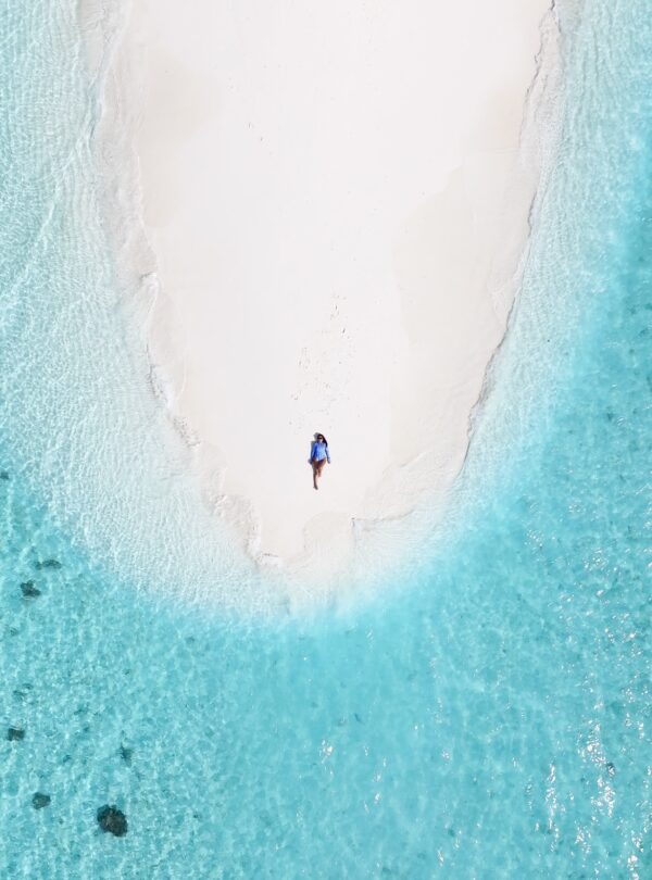 Mujer acostada en una pequeña isla de arena blanca rodeada de aguas cristalinas vistas desde un ángulo aéreo