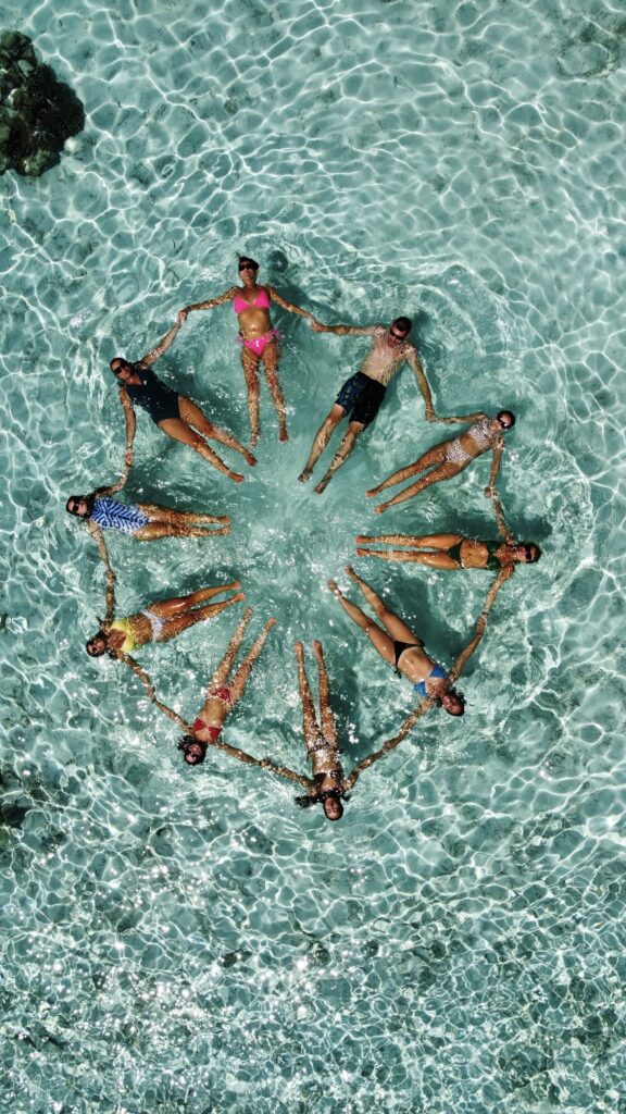 Grupo de personas flotando en aguas cristalinas y formando un círculo mientras se toman de las manos.
