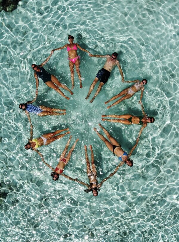 Grupo de personas flotando en aguas cristalinas y formando un círculo mientras se toman de las manos.