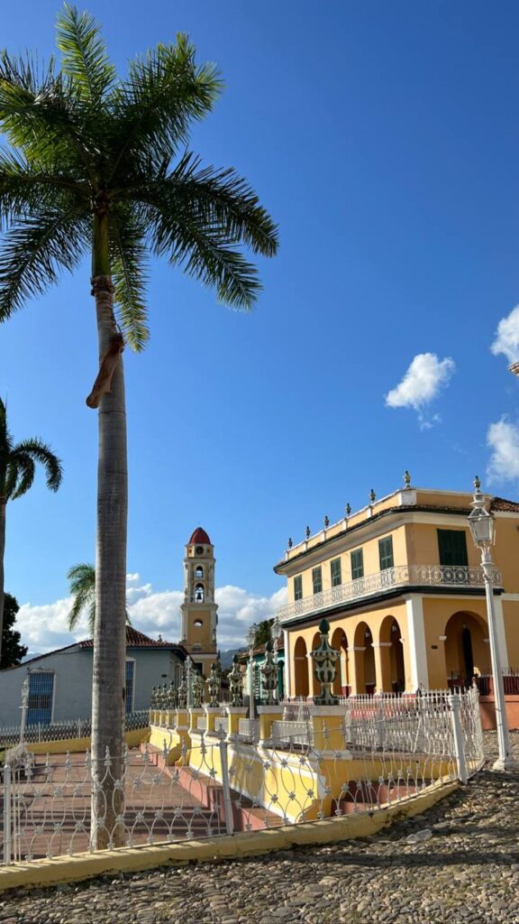 Calle empedrada en un pueblo colonial con edificios coloridos y una torre de iglesia al fondo, bajo un cielo azul despejado.