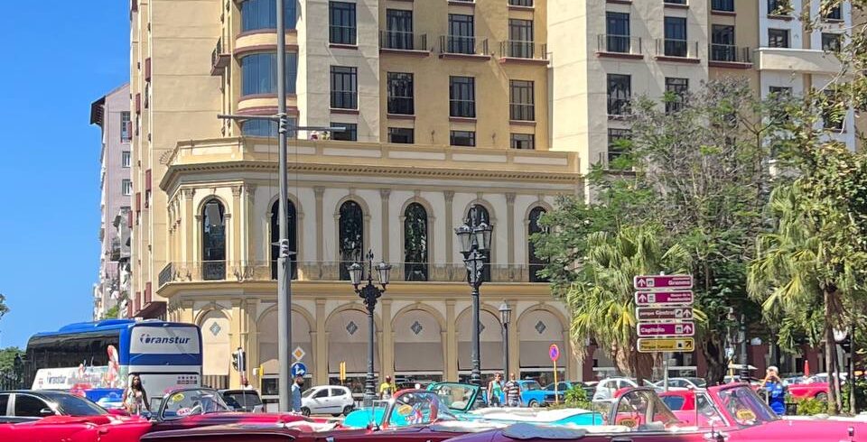 Autos clásicos descapotables de colores vibrantes estacionados en una calle de La Habana, con el Hotel Iberostar Parque Central de fondo.