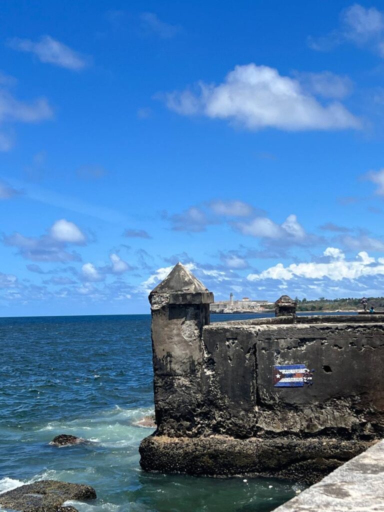 Antigua fortificación en la costa de La Habana con el mar azul de fondo y una bandera de Cuba pintada en la pared
