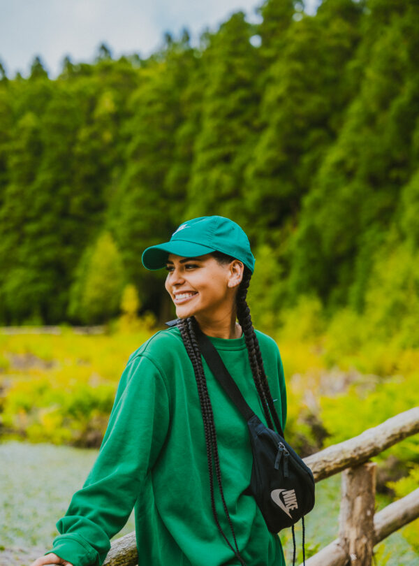 Mujer sonriente con ropa verde y gorra disfrutando de un entorno natural lleno de vegetación en las Azores.