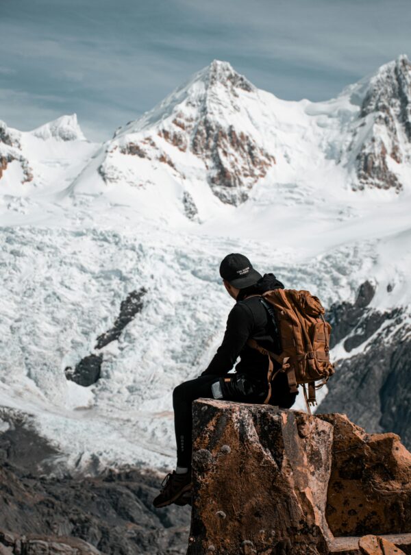 Hombre con mochila sentado en una roca contemplando montañas nevadas y un glaciar.
