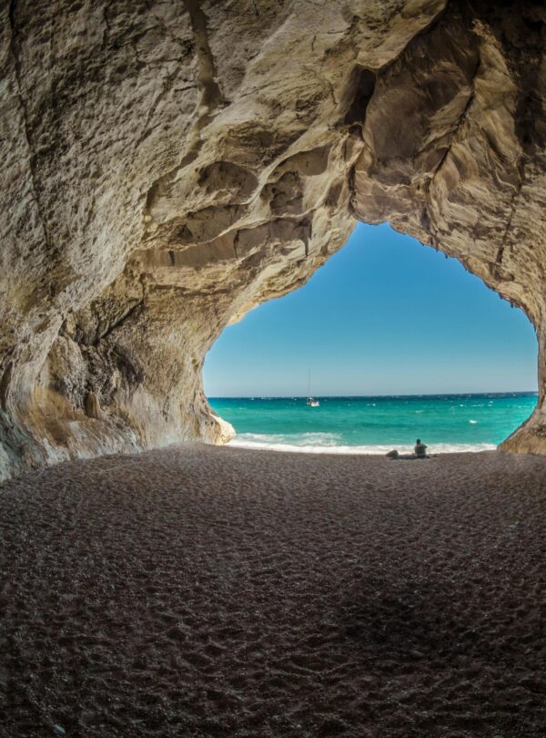 Vista desde el interior de una cueva hacia una playa de aguas turquesas con una persona disfrutando del paisaje.