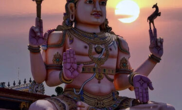 Estatua gigante del dios hindú Shiva con el sol poniéndose detrás de ella, en un entorno de templo.