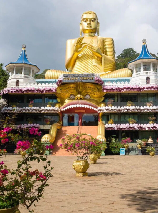 Estatua gigante dorada de Buda en el Templo Dorado de Dambulla, Sri Lanka, con un edificio decorado y torres azules a sus lados.