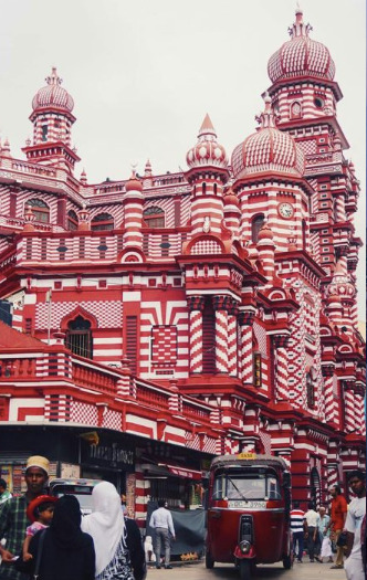 Mezquita Jami Ul-Alfar en Colombo, Sri Lanka, con arquitectura islámica en tonos rojos y blancos y personas caminando por la calle.