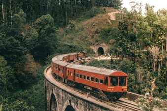 Tren rojo cruzando el Puente de los Nueve Arcos rodeado de vegetación en las colinas de Ella, Sri Lanka.