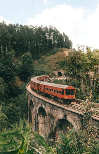 Tren rojo cruzando el Puente de los Nueve Arcos rodeado de vegetación en las colinas de Ella, Sri Lanka.