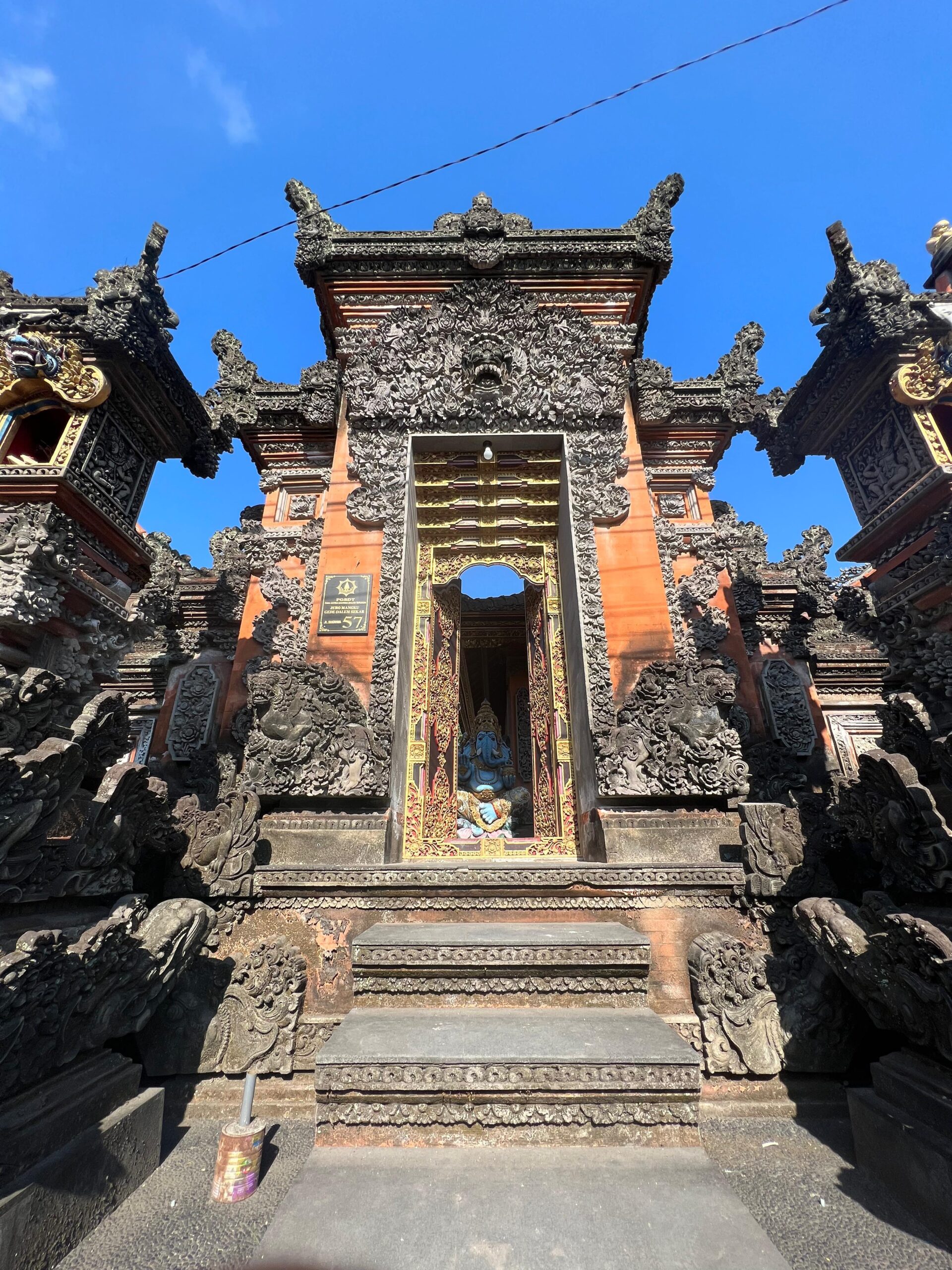 Entrada tallada de un templo hindú tradicional en Bali, con esculturas ornamentadas y una estatua azul visible en el interior.
