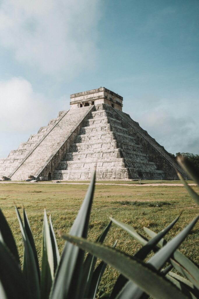 Pirámide de Chichén Itzá en México con plantas en primer plano y cielo despejado al fondo.
