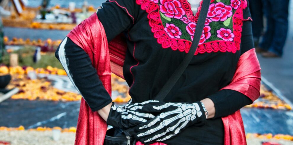 Mujer disfrazada de Catrina con maquillaje tradicional y vestimenta colorida durante celebración del Día de Muertos en México.