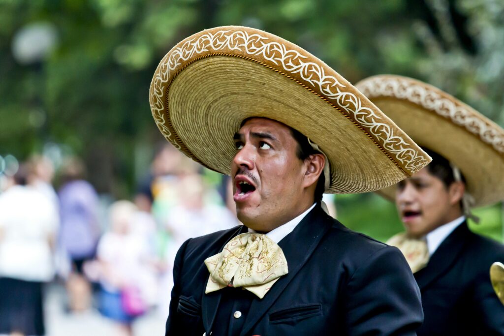 Mariachi mexicano cantando con sombrero charro y traje tradicional durante una presentación al aire libre.