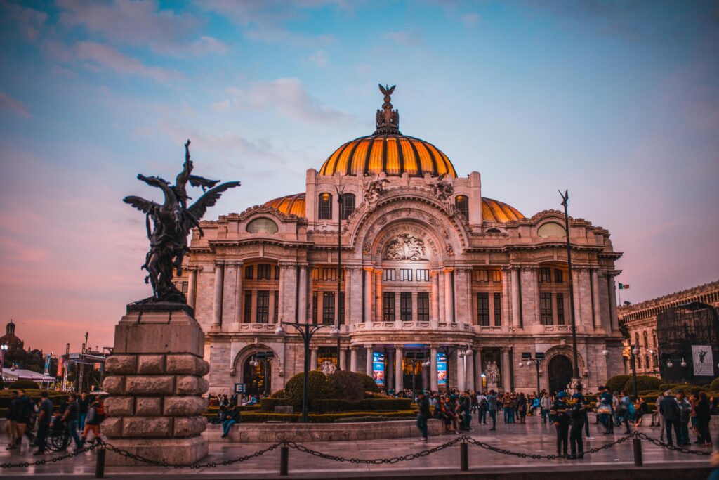 Palacio de Bellas Artes iluminado al atardecer en la Ciudad de México, con personas caminando alrededor.