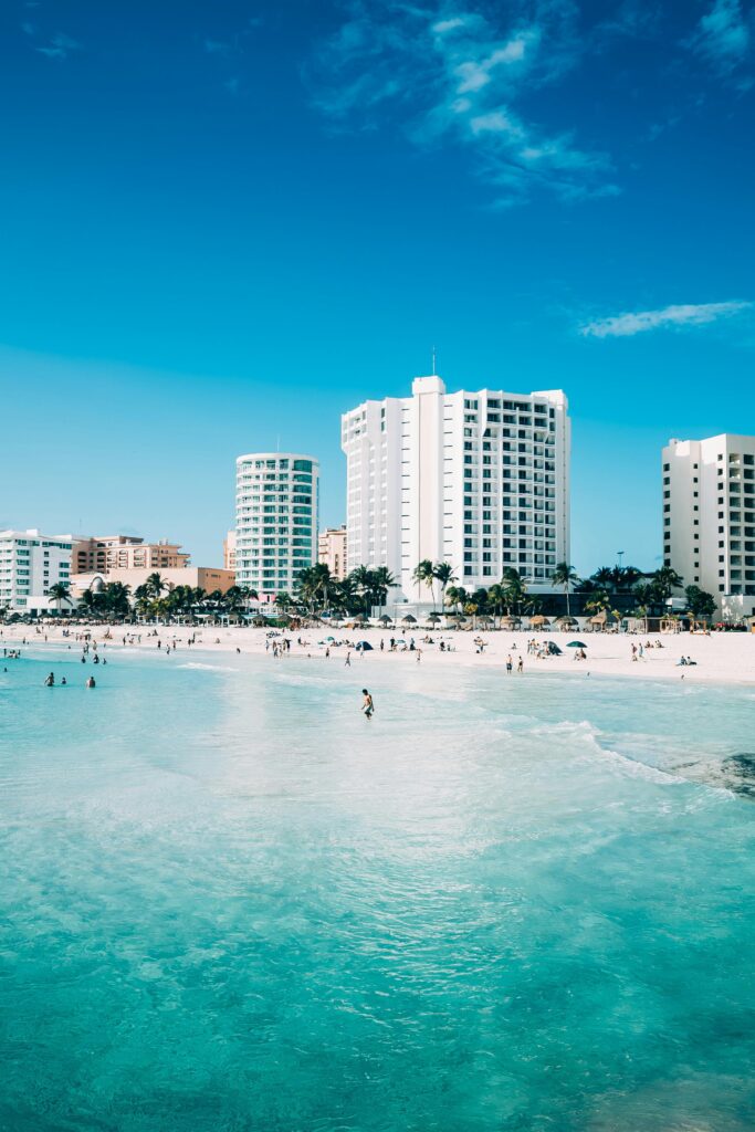 Playa con mar turquesa y hoteles de gran altura al fondo en un día soleado.