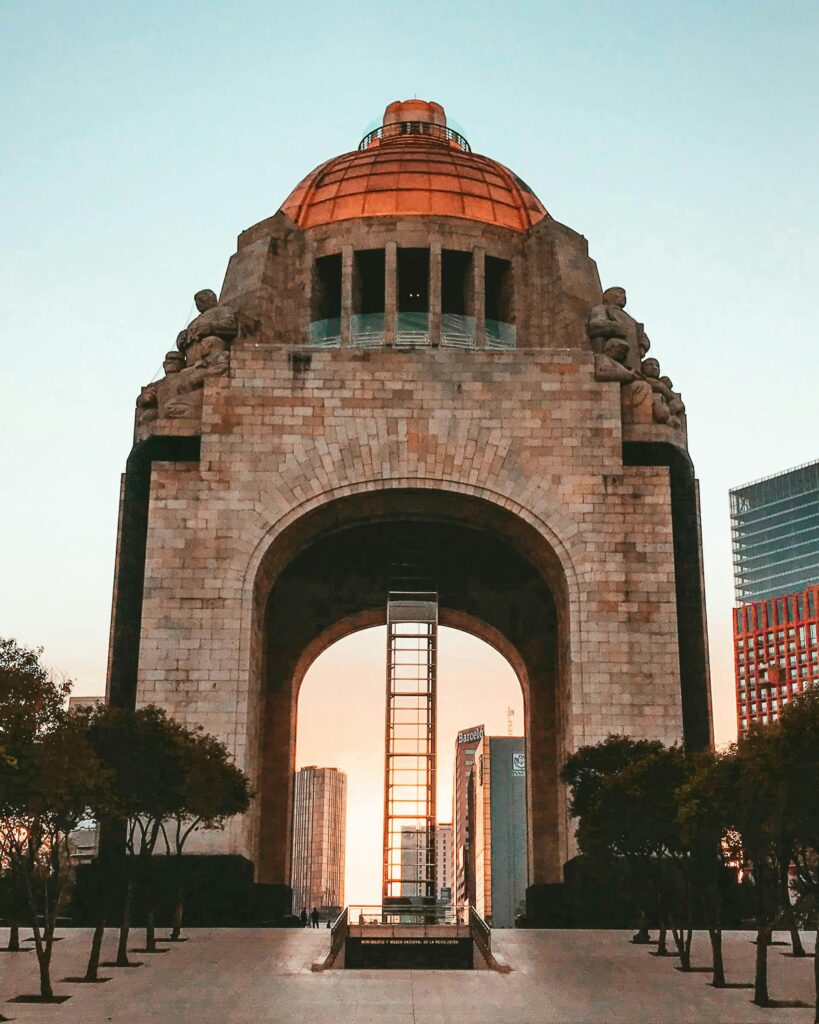 Monumento a la Revolución Mexicana al atardecer con edificios modernos al fondo.