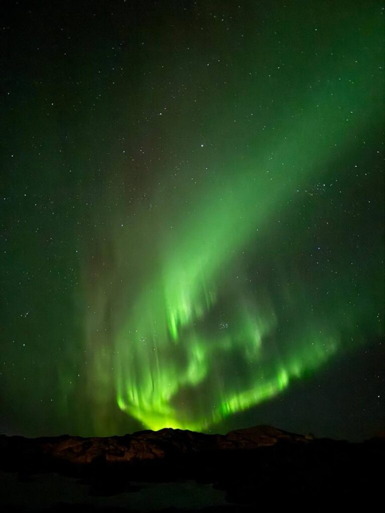 Espectacular aurora boreal verde iluminando el cielo nocturno estrellado sobre un paisaje montañoso oscuro.