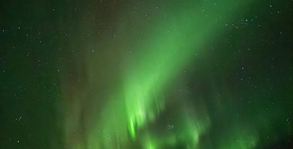 Espectacular aurora boreal verde iluminando el cielo nocturno estrellado sobre un paisaje montañoso oscuro.