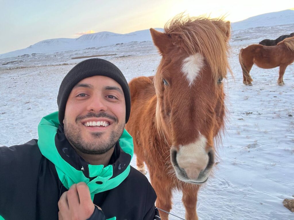 Hombre sonriendo junto a un caballo islandés marrón con una mancha blanca en la frente, en un paisaje nevado.