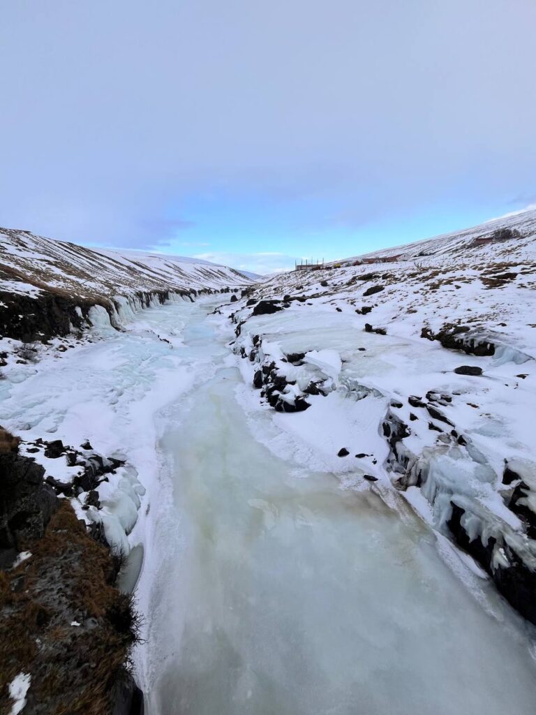 Río completamente congelado serpenteando entre colinas nevadas bajo un cielo invernal.