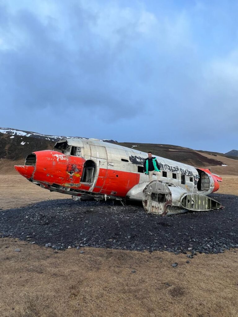 Hombre posando sobre los restos de un avión militar estadounidense estrellado en un paisaje desértico de Islandia.