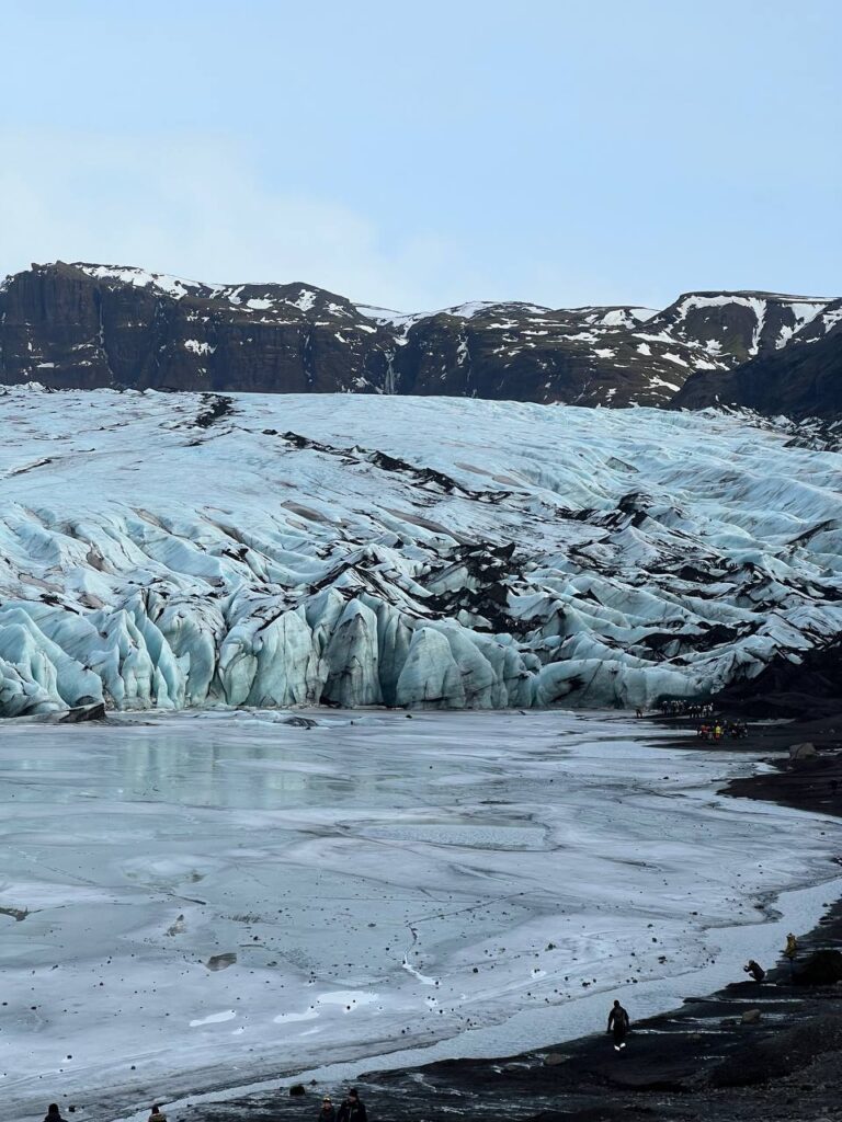 Glaciar con hielo azul y superficie congelada en primer plano, rodeado de montañas oscuras con nieve.