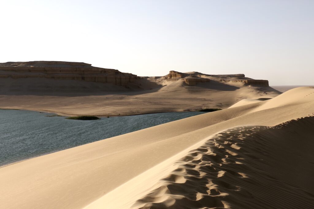 Oasis en medio del desierto con dunas de arena y una masa de agua azul en el Valle de las Ballenas, Egipto.
