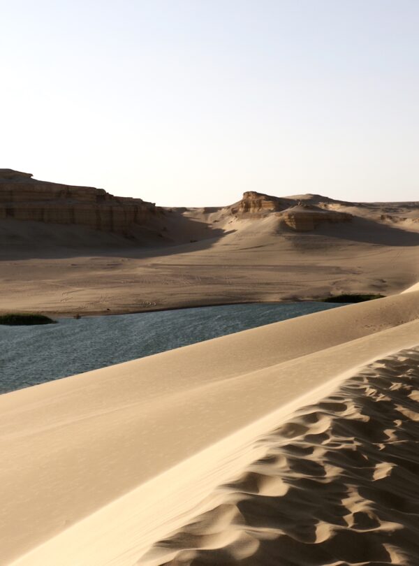 Oasis en medio del desierto con dunas de arena y una masa de agua azul en el Valle de las Ballenas, Egipto.