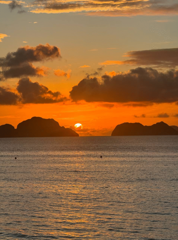 Atardecer sobre el mar con el sol ocultándose entre formaciones rocosas en el horizonte.