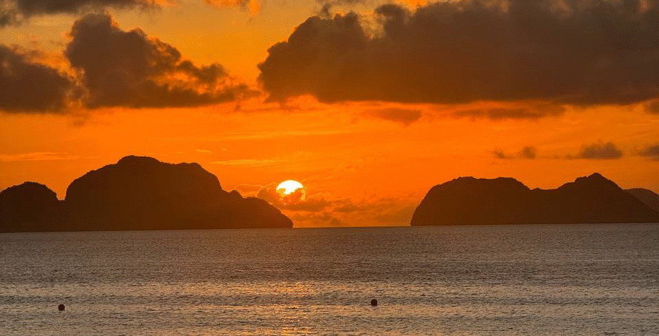 Atardecer sobre el mar con el sol ocultándose entre formaciones rocosas en el horizonte.