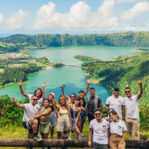 Grupo de personas sonrientes posando frente a la Laguna de las Siete Ciudades en las Azores, Portugal, con un paisaje verde y montañoso al fondo.