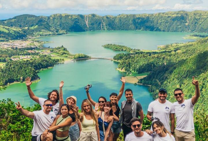 Grupo de personas sonrientes posando frente a la Laguna de las Siete Ciudades en las Azores, Portugal, con un paisaje verde y montañoso al fondo.