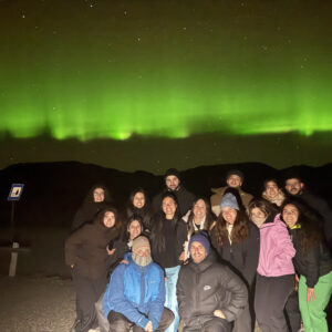 Grupo de personas posando sonrientes bajo una aurora boreal verde en una noche estrellada.