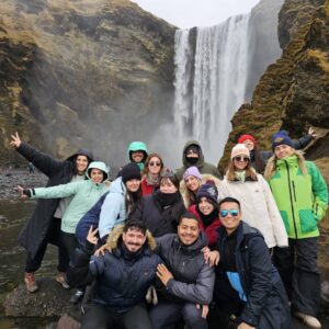 Grupo de personas posando frente a una gran cascada rodeada de montañas cubiertas de musgo.