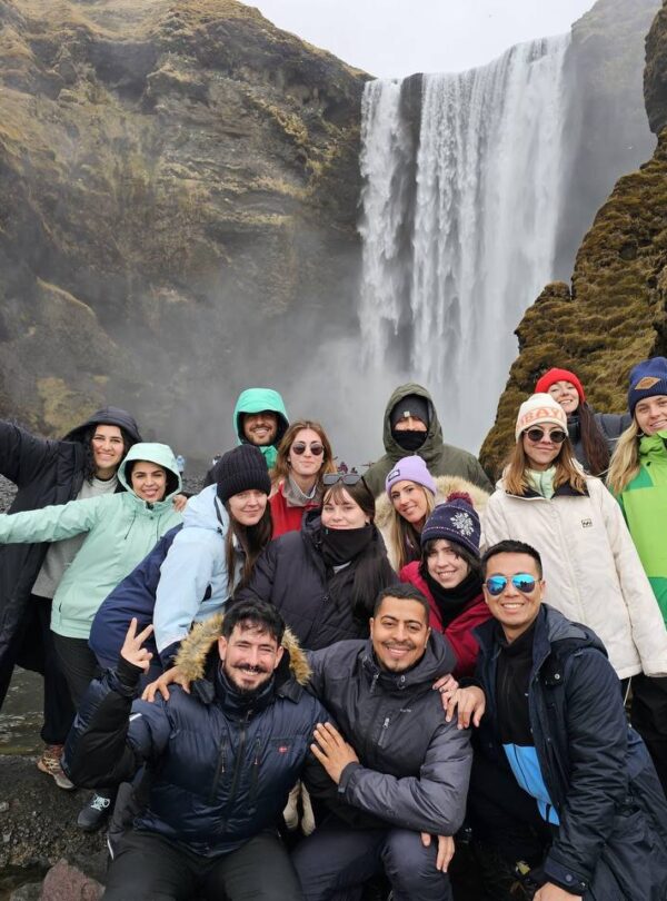 Grupo de personas posando frente a una gran cascada rodeada de montañas cubiertas de musgo.