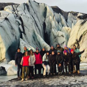 Grupo de personas posando frente a un glaciar con grandes bloques de hielo y montañas al fondo.