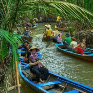 Personas navegando en pequeñas barcas de remo a través de un canal rodeado de vegetación tropical densa, posiblemente en el delta del Mekong, Vietnam.