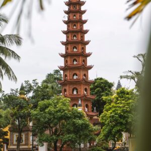 Pagoda Trấn Quốc en Hanói, Vietnam, con su torre roja de múltiples niveles rodeada de árboles tropicales y reflejada en un estanque.