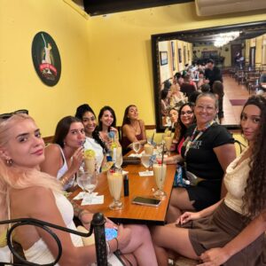 Grupo de mujeres sentadas alrededor de una mesa en un restaurante, disfrutando bebidas frías decoradas con sombrillitas.