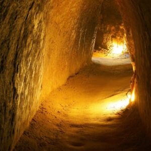 Túnel subterráneo iluminado con luces cálidas, excavado en tierra firme.