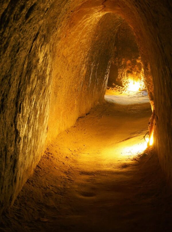 Túnel subterráneo iluminado con luces cálidas, excavado en tierra firme.