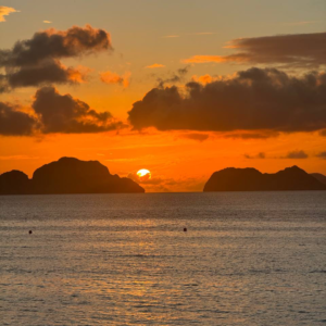Atardecer naranja sobre el mar con el sol ocultándose entre dos islas y nubes oscuras en el cielo.